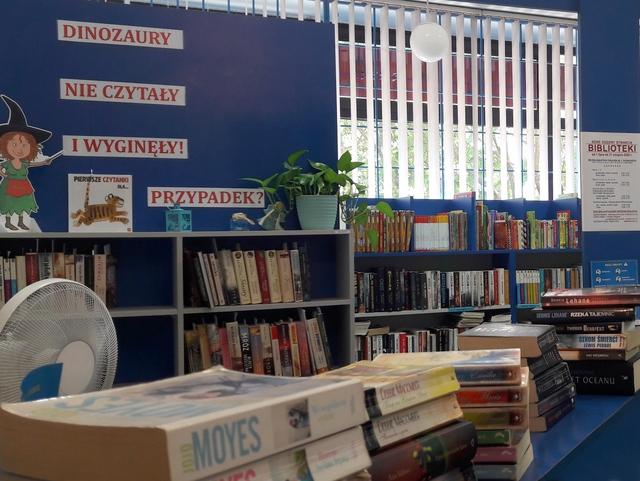 Stanowisko do obsługi czytelnika. W tle na niebieskim tle napis: "Dinozaury nie czytały i wyginęły! Przypadek?".