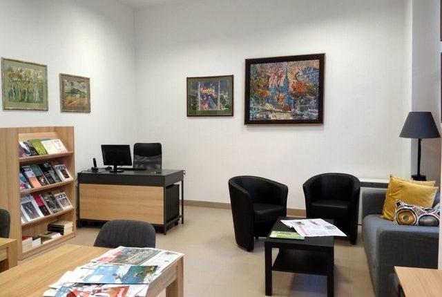 Pomieszczenie z biurkiem, fotelami i sofą. Na ścianie obrazy. Niski regał z książkami