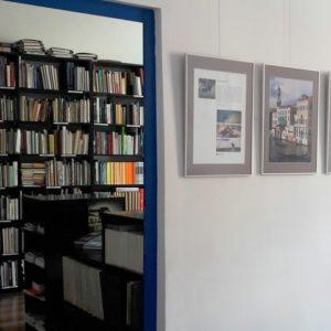 Fragment wystawy fotograficznej. Przez otwarte drzwi widoczna pracownia z księgozbiorem.