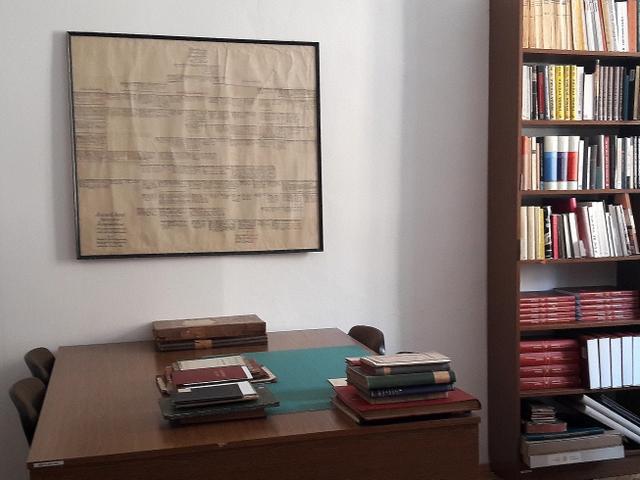 Czytelnia działu z fragmentem regału, stołem z książkami i oprawionym rękopiśmiennym dokumentem na ścianie