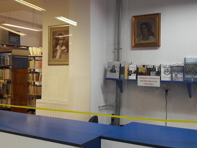Stanowisko do obsługi czytelnika. W tle portret Juliusza Słowackiego i półka z wydawnictwami biblioteki.