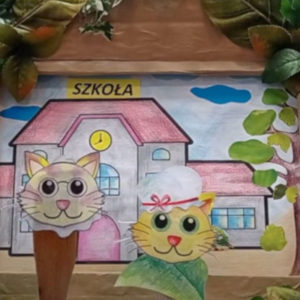 Fragment teatrzyku - w tle budynek, na pierwszym planie dwa kotki wycinanki.