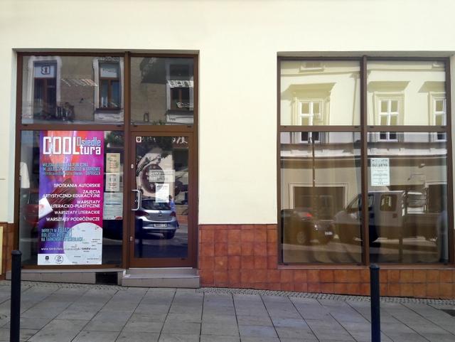 Widok na witrynę czytelni czasopism bieżących. Z lewej strony duży plakat Cooltura Osiedle