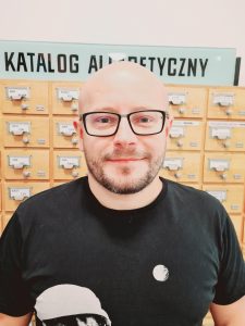 Mężczyzna w okularach na tle bibliotecznej szafki katalogowej