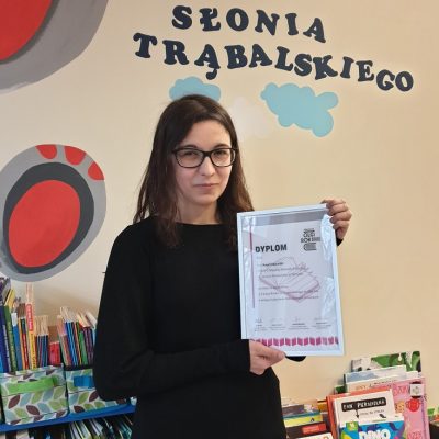 Na tle książek i napisu Kącik Słonia Trąbalskiego długowłosa kobieta trzymająca dyplom