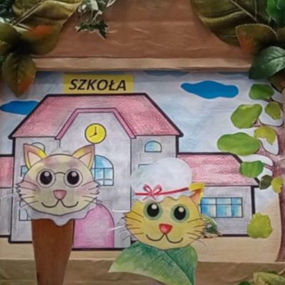 Fragment teatrzyku - w tle budynek, na pierwszym planie dwa kotki wycinanki.