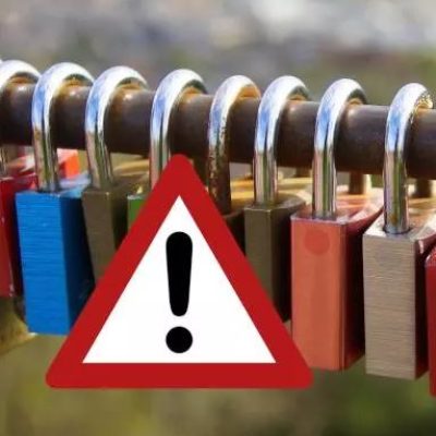 Biblioteka nieczynna Na poziomo ustawionym pręcie wiszą zamknięte kolorowe kłódki. Na ich tle znak wykrzyknika w czerwonym ostrzegawczym trójkącie.